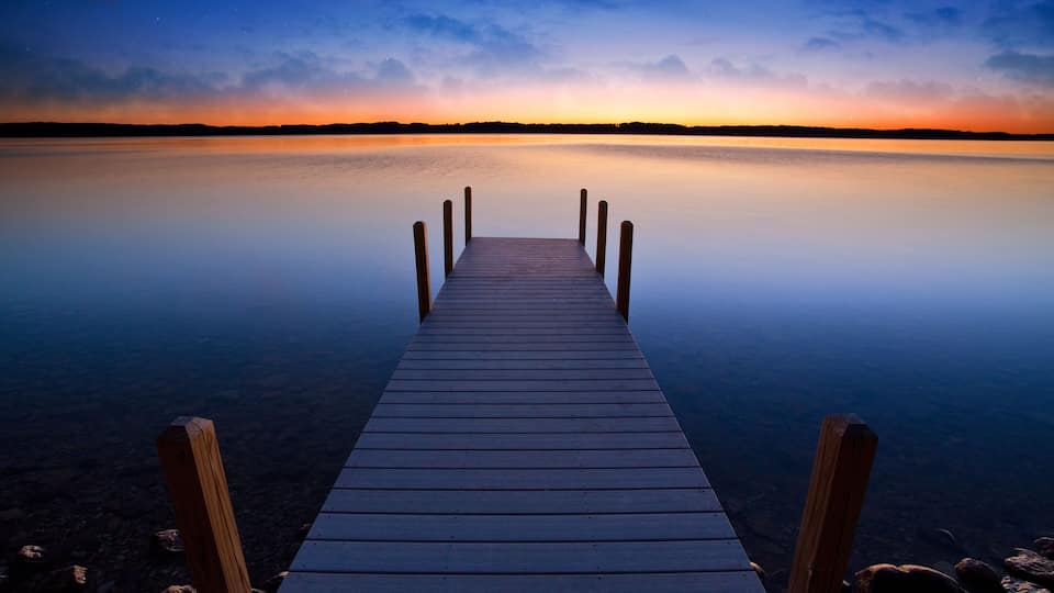 A wooden pier extending into calm water with a sunset sky.