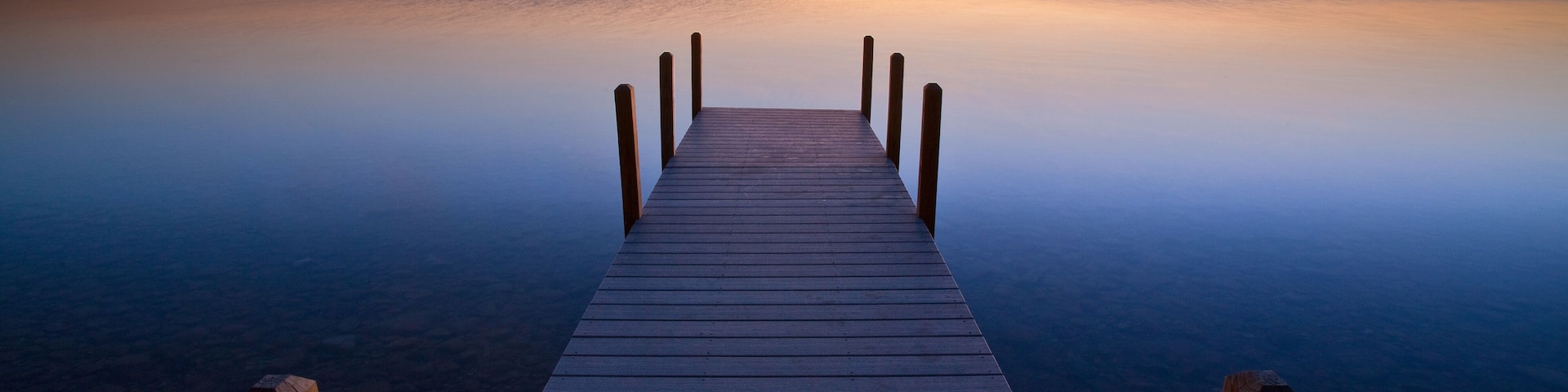 Un muelle de madera que se adentra en aguas tranquilas bajo un cielo al atardecer.