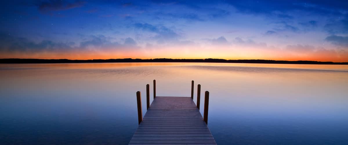 A wooden pier extending into calm water with a sunset sky.