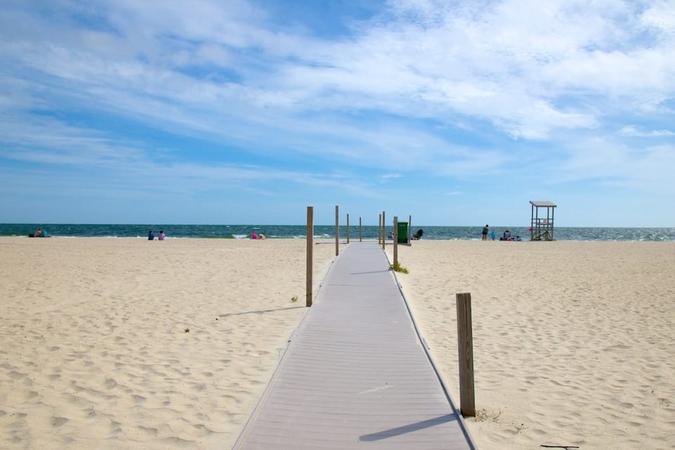 Ein Sandstrand mit einem hölzernen Steg, der zum Meer führt.