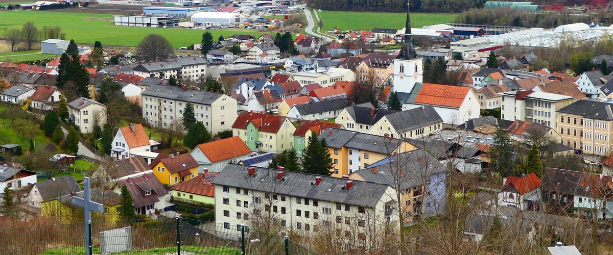 A town with colorful houses, a church, and mountains in the background.