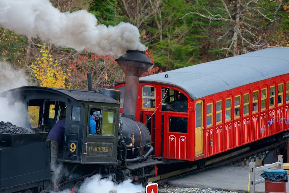 Ett ånglok med nummer 9, som släpper ut ånga, drar en röd passagerarvagn med texten ”Mt. Washington” på.