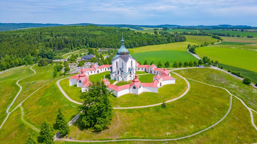 Vue aérienne d’un vaste complexe religieux, entouré de champs verdoyants et de forêts.