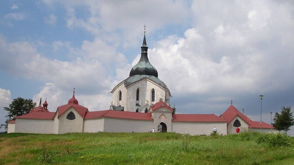 A church with a green dome and red roof, surrounded by green grass and trees.