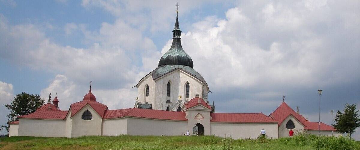 Eine Kirche mit einer grünen Kuppel und einem roten Dach, umgeben von grünem Gras und Bäumen.
