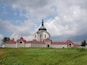 A church with a green dome and red roof, surrounded by green grass and trees.