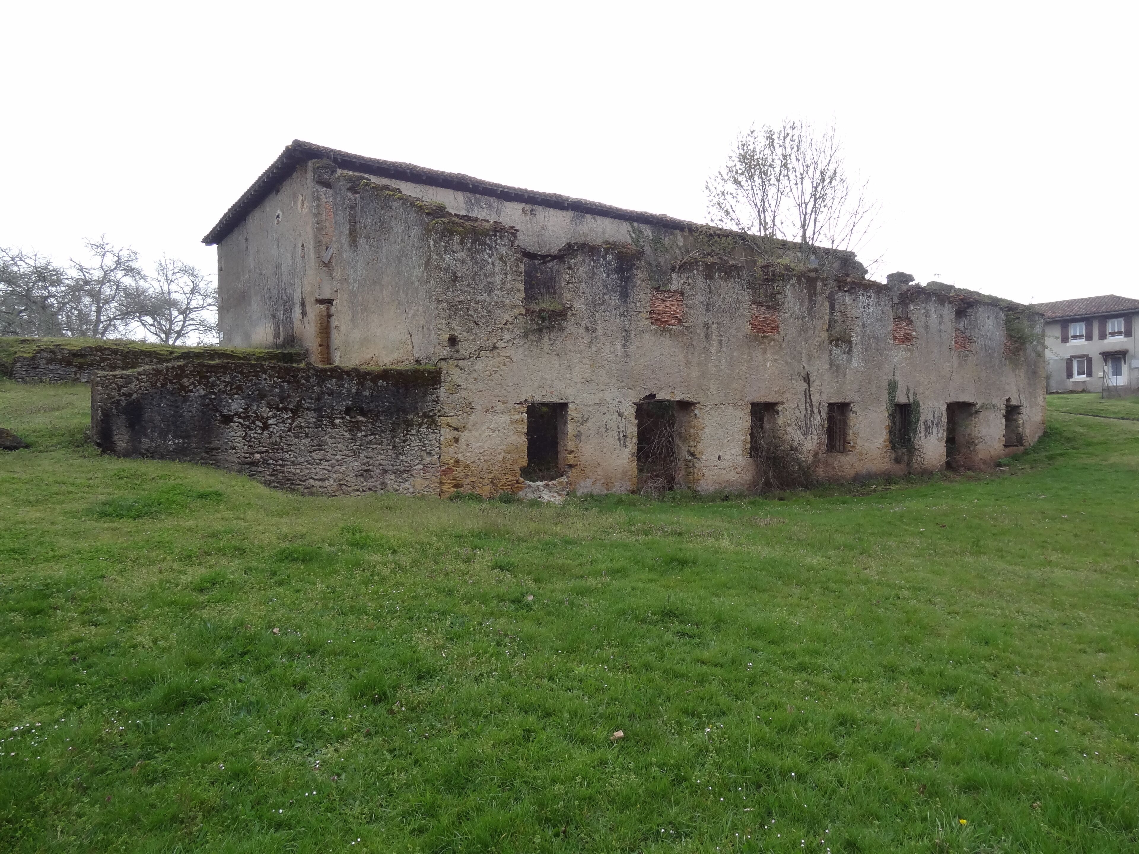 An old, weathered building with a stone base and multiple windows, surrounded by a grassy field.