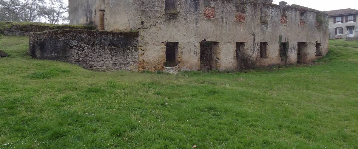 An old, weathered building with a stone base and multiple windows, surrounded by a grassy field.