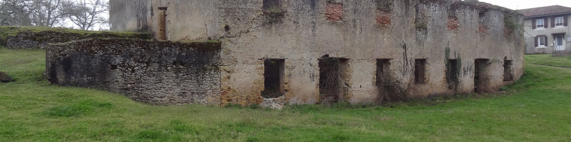 An old, weathered building with a stone base and multiple windows, surrounded by a grassy field.