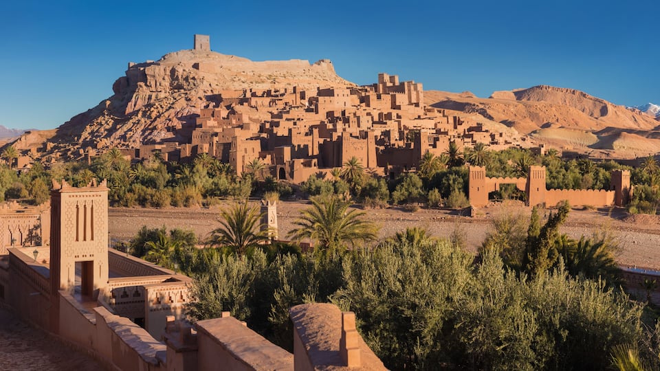 A desert landscape with a prominent mountain and a fortified town with traditional architecture.