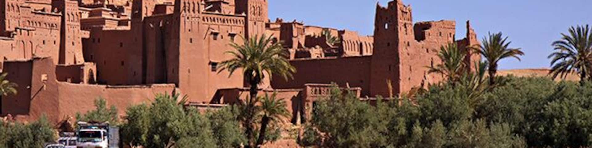 A desert landscape with a large adobe building, palm trees, and a truck.