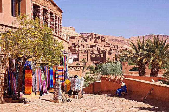 A traditional market with colorful textiles, a palm tree, and a person working on a wall.