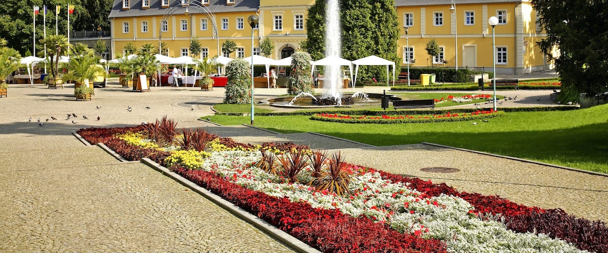 A yellow building with a fountain in front, surrounded by a landscaped garden with red and white flowers.