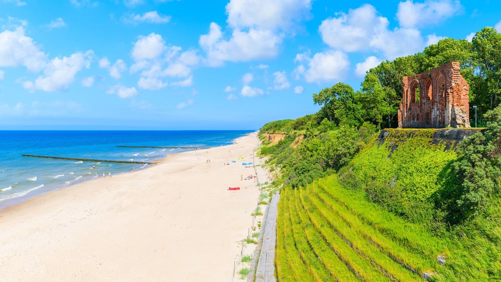 Une plage avec une structure historique en briques, située sur une colline verdoyante.