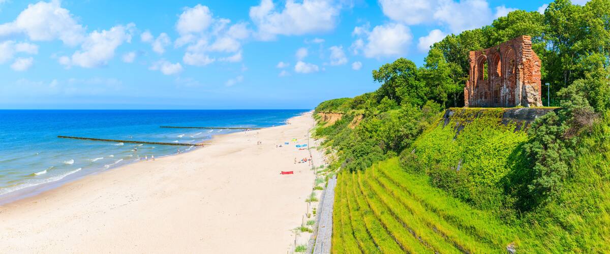 A beach with a historic brick structure on a grassy hill.