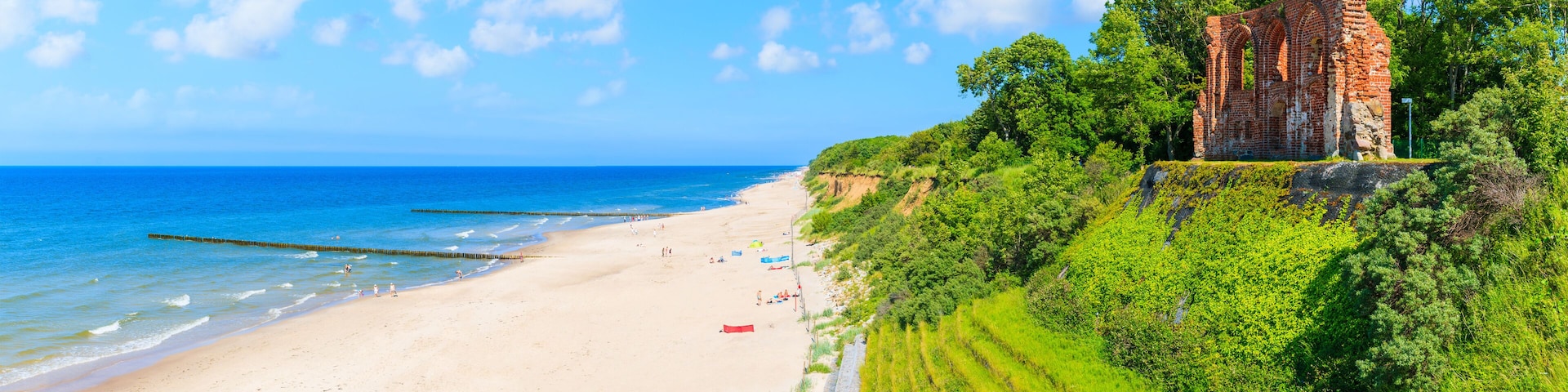 A beach with a historic brick structure on a grassy hill.