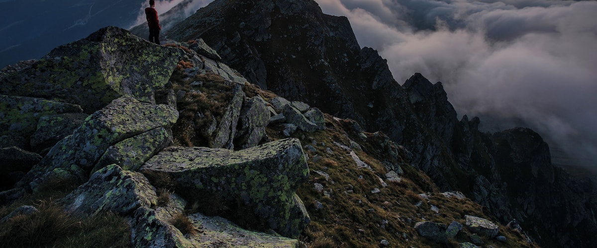 A person standing on a rocky mountain peak with a sunset in the background.