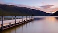 Une jetée en bois s’étendant sur un lac paisible, entourée de montagnes et surplombant un ciel dégagé.