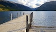 Un muelle de madera que se adentra en un lago tranquilo, rodeado de montañas.
