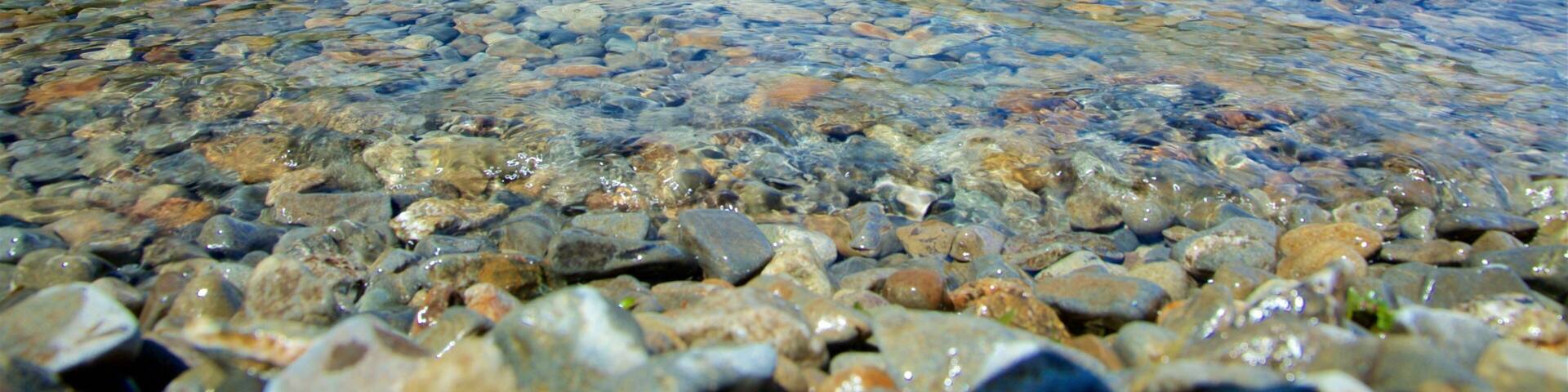 A clear lake with visible pebbles and mountains in the background.
