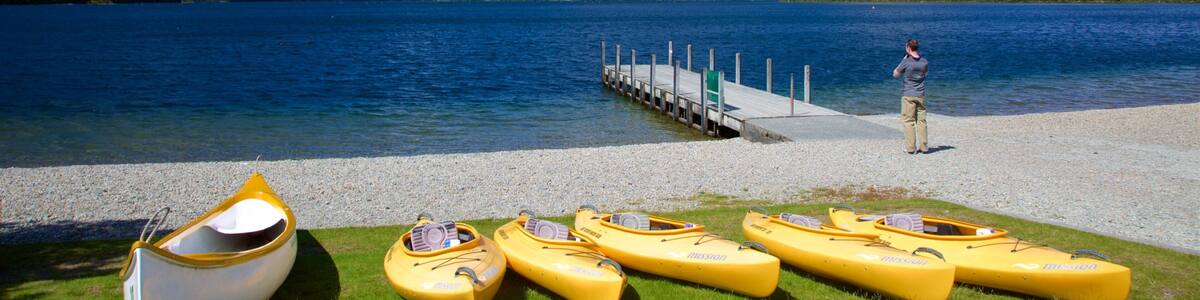 A lake with mountains in the background, a dock, and several yellow kayaks on the shore.