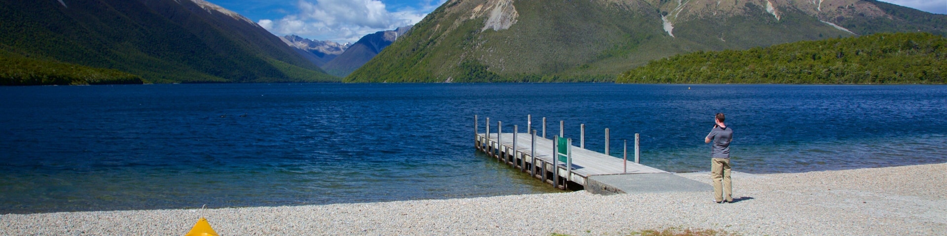 Um lago com montanhas ao fundo, um cais e vários caiaques amarelos na margem.