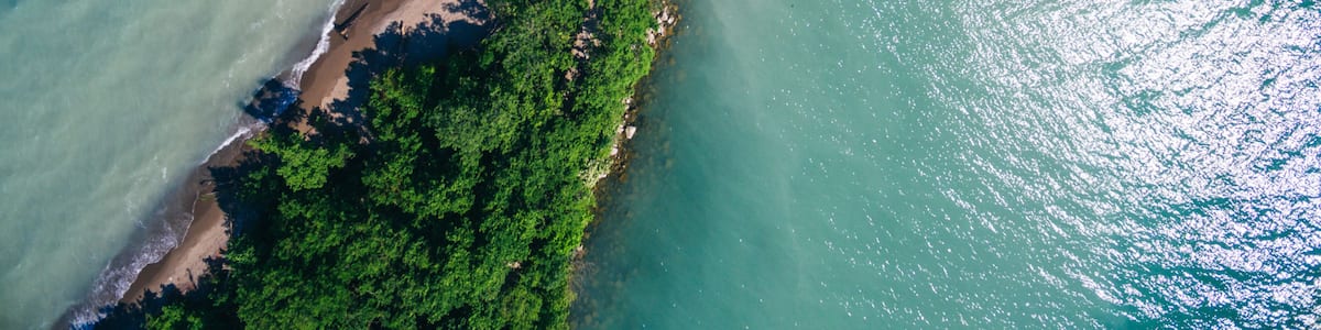 An aerial view of a coastal area with clear turquoise waters, a sandy beach, and dense green vegetation along the shoreline.