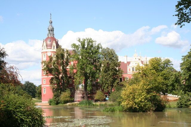 A historic building with a tower, surrounded by lush greenery and a pond.