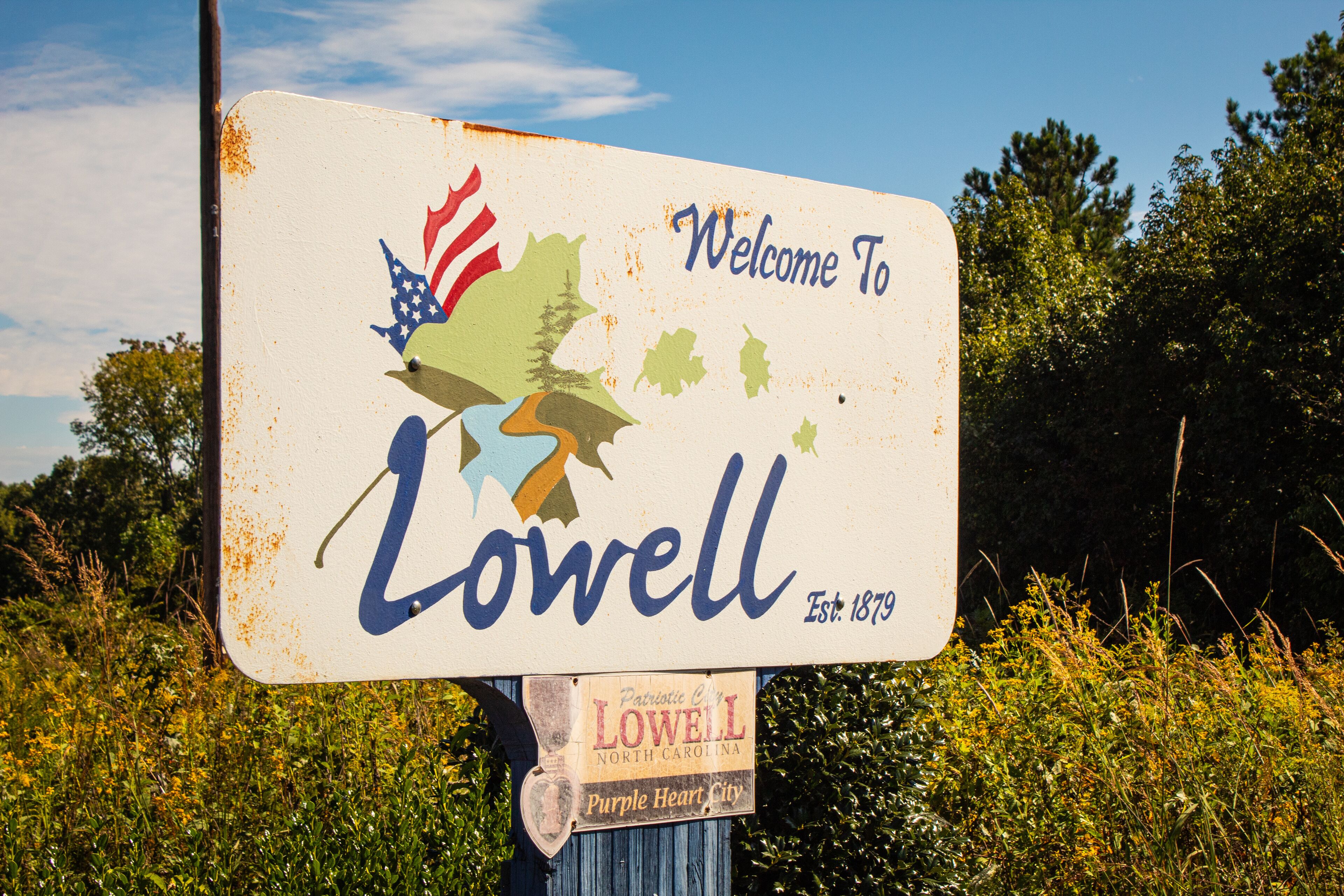 A weathered welcome sign for Lowell, North Carolina, with a map and American flag.