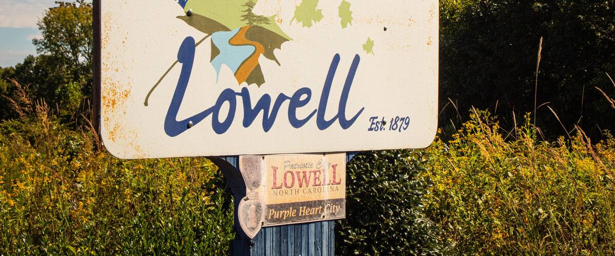 A weathered welcome sign for Lowell, North Carolina, with a map and American flag.