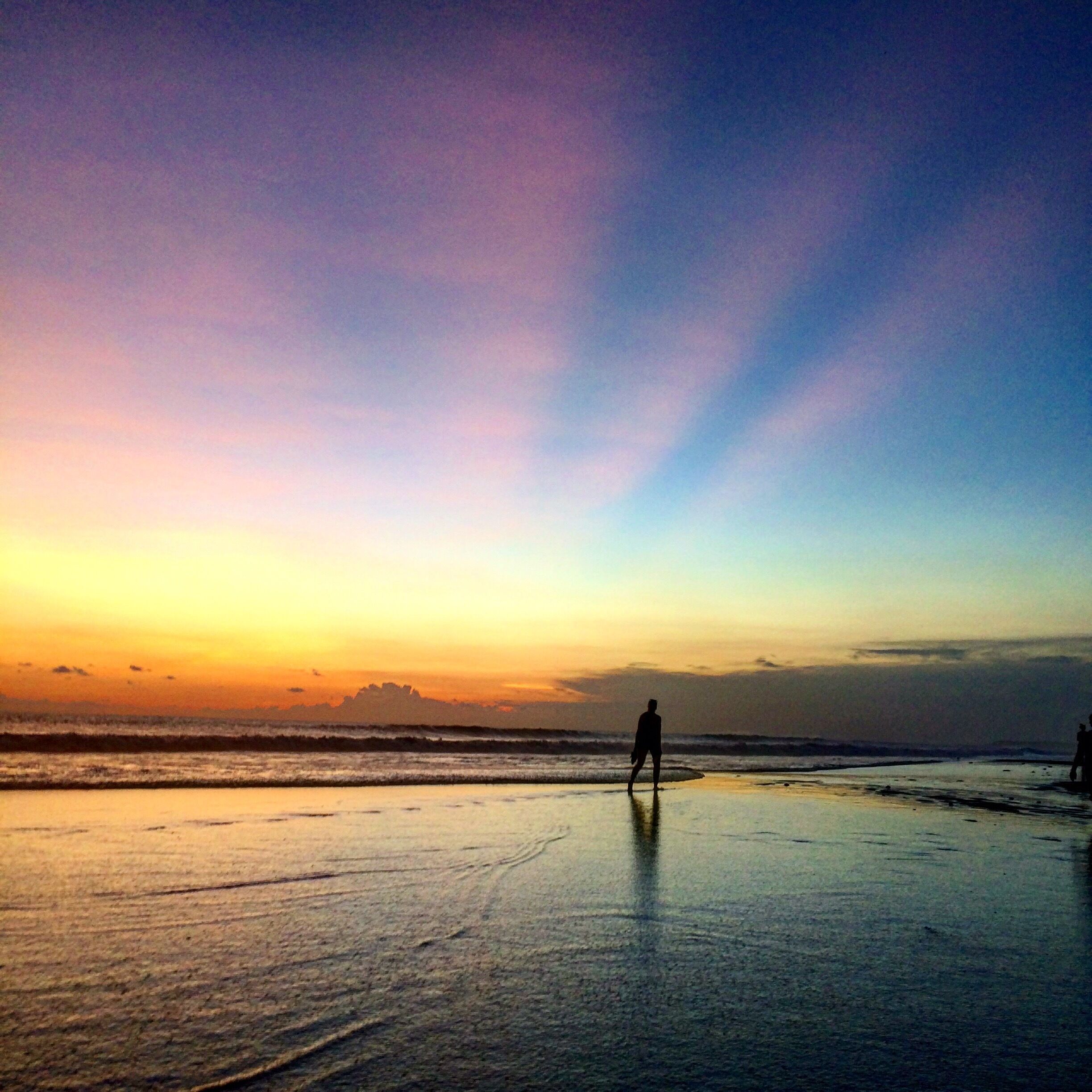 A beach at sunset with a person standing on the shore.