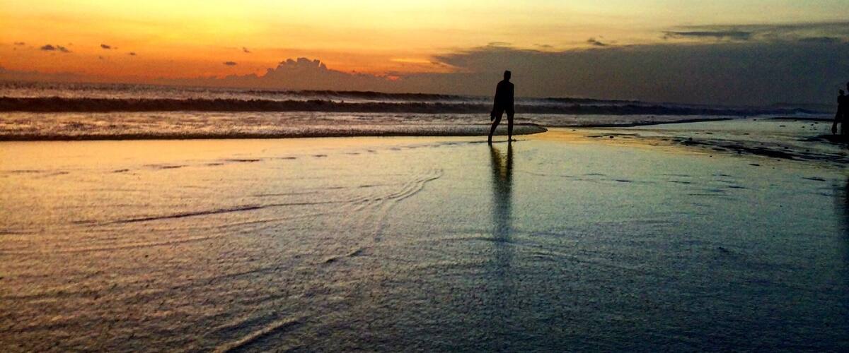 A beach at sunset with a person standing on the shore.