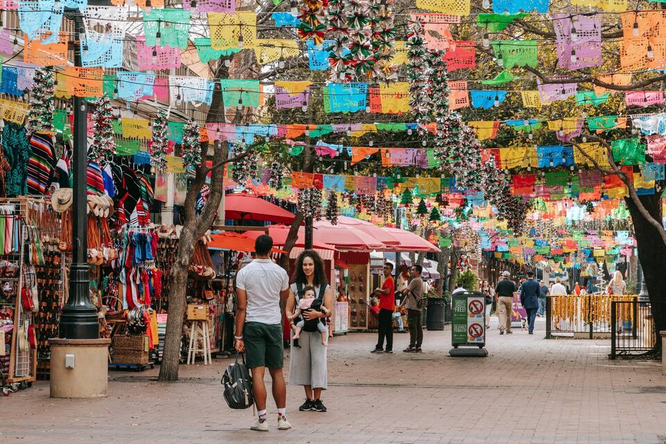 A vibrant street market with colorful papel picado banners, stalls selling handicrafts, and a festive atmosphere.