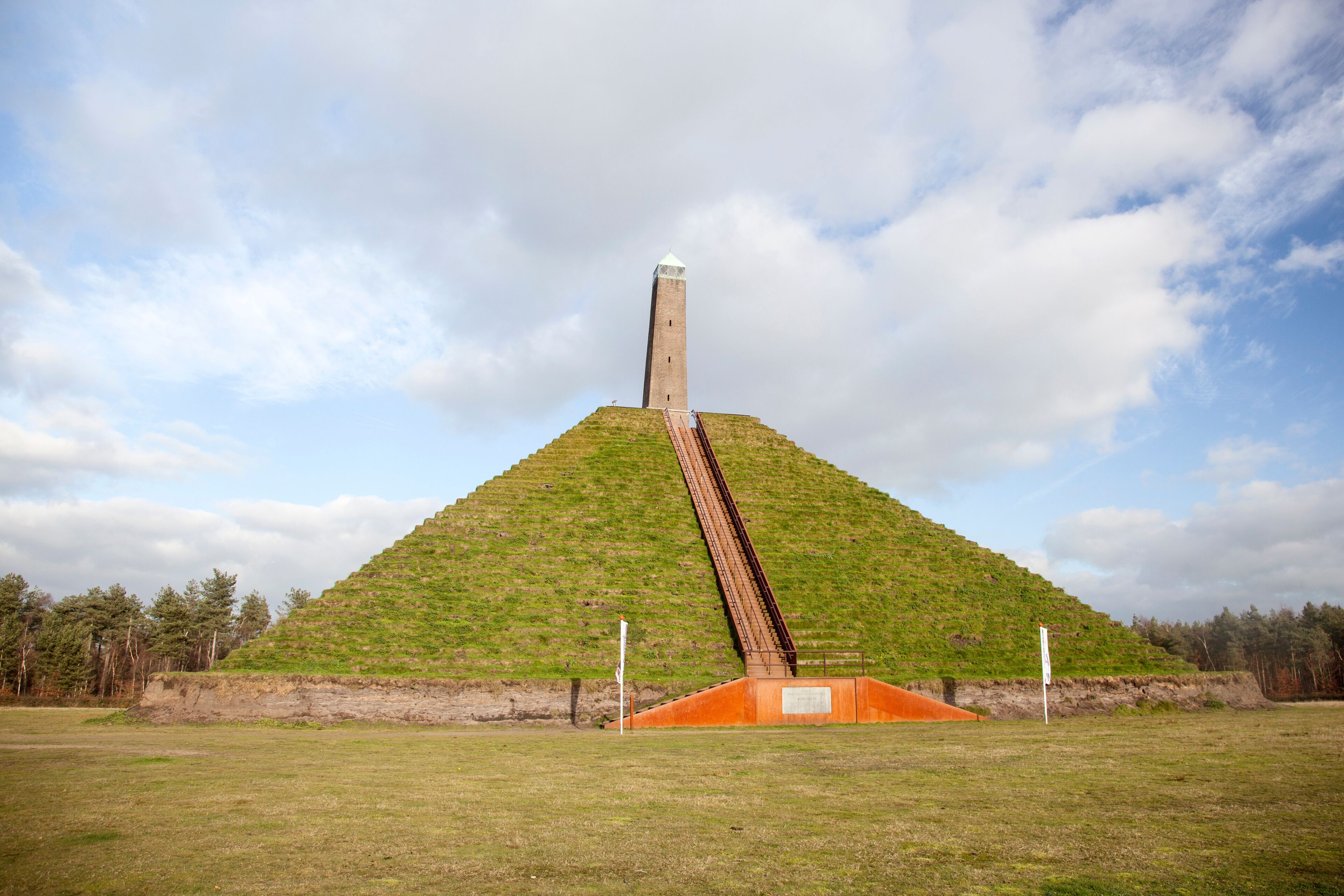A large pyramid-like structure with a tall central tower, surrounded by a grassy field and trees.
