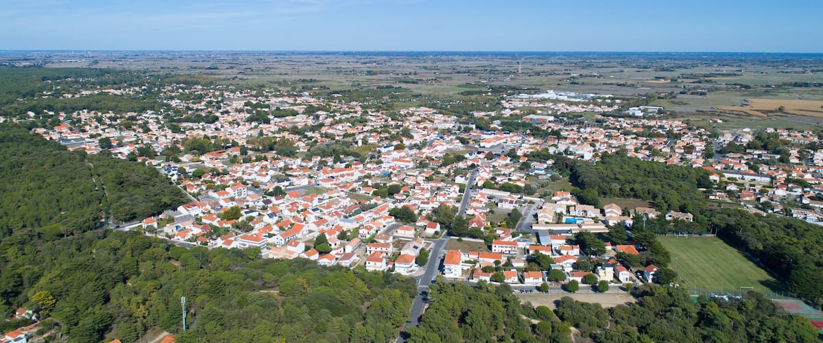 A densely populated town with red-roofed houses, surrounded by green fields and trees.