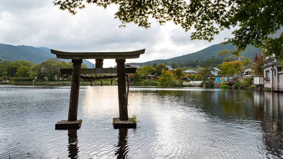 A traditional Japanese torii gate in a body of water, surrounded by mountains and a small village.