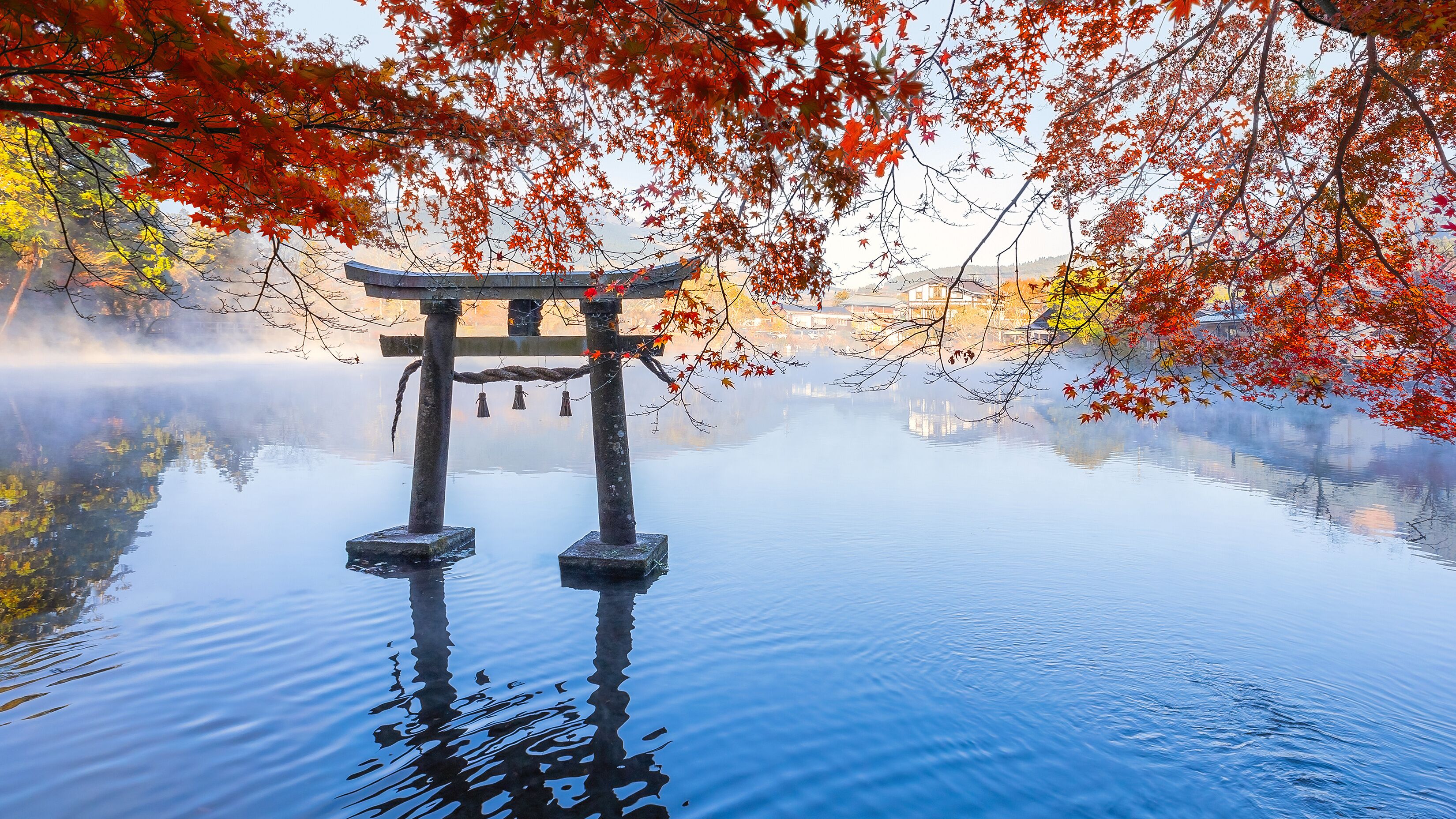 A serene water body with a traditional Japanese torii gate in the foreground, surrounded by autumn foliage.
