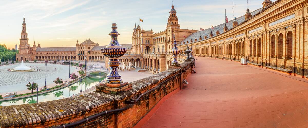A historic plaza with a fountain, ornate buildings, and a long colonnade.