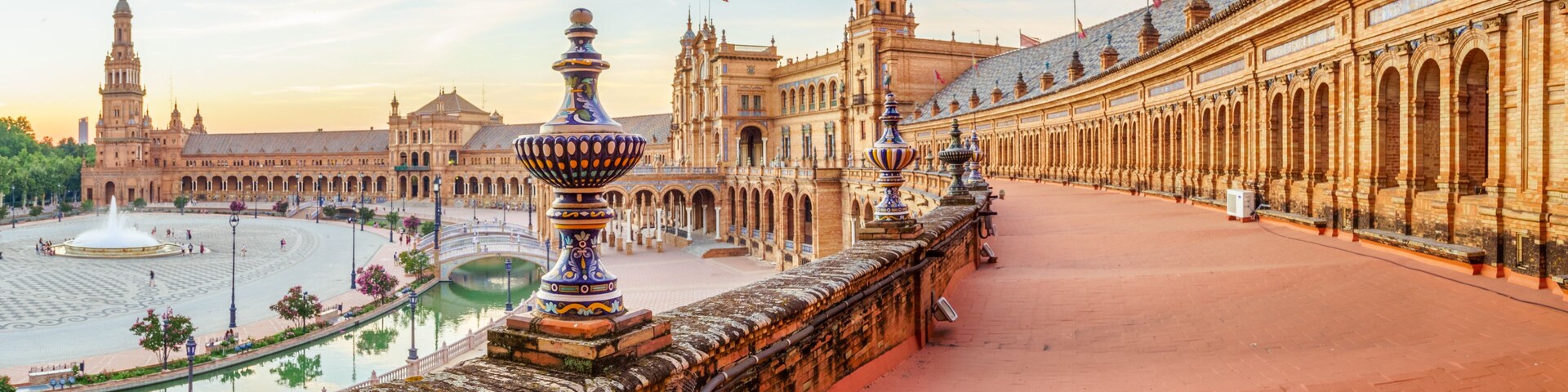 Una plaza histórica con una fuente, edificios ornamentados y una larga columnata.