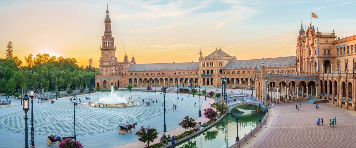 A historic plaza with a fountain, ornate buildings, and a clear sky.