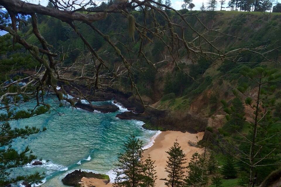 Paesaggio costiero con spiaggia sabbiosa, acque color turchese e vegetazione circostante.