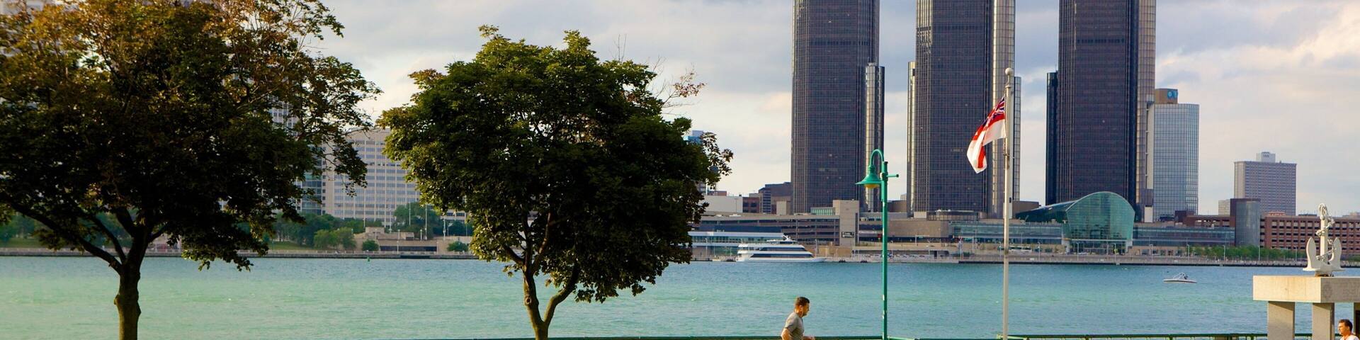 A park with a river, a man jogging, and a city skyline with tall buildings in the background.