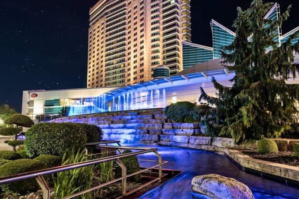 A nighttime view of a hotel with a moon in the sky, a waterfall, and illuminated steps leading to the building.