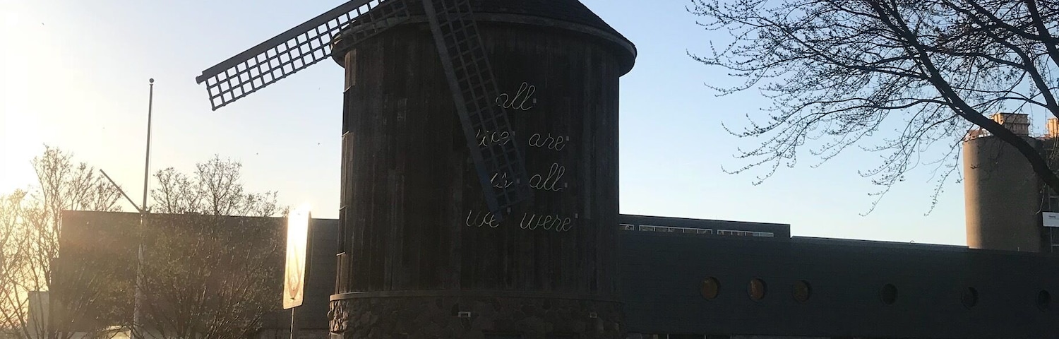 Eine Windmühle mit Beschriftung, eine Wiese und ein Gebäude im Hintergrund.