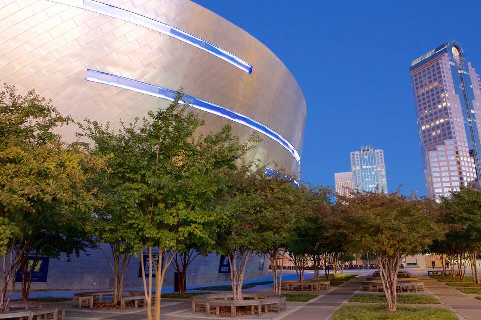 A modern building with a curved facade and blue lighting, surrounded by trees and benches in a park setting.