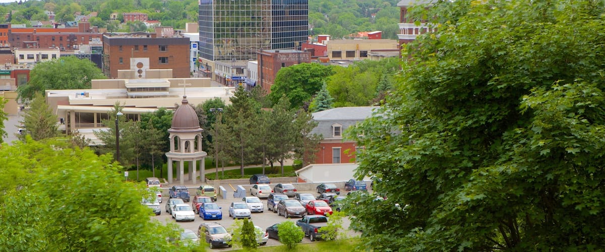 A cityscape with a mix of modern and historic buildings, a parking lot, and lush green trees.