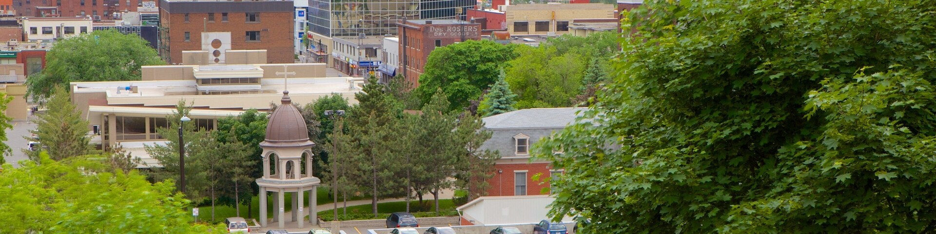 A cityscape with a mix of modern and historic buildings, a parking lot, and lush green trees.