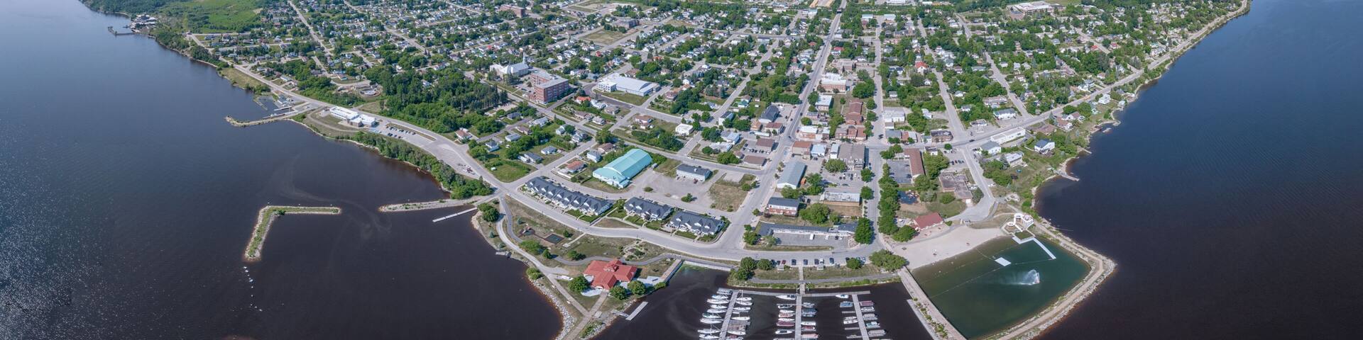 An aerial view of a coastal town with a marina, dense residential area, and surrounding greenery.