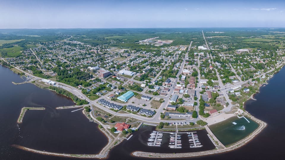 An aerial view of a coastal town with a marina, dense residential area, and surrounding greenery.