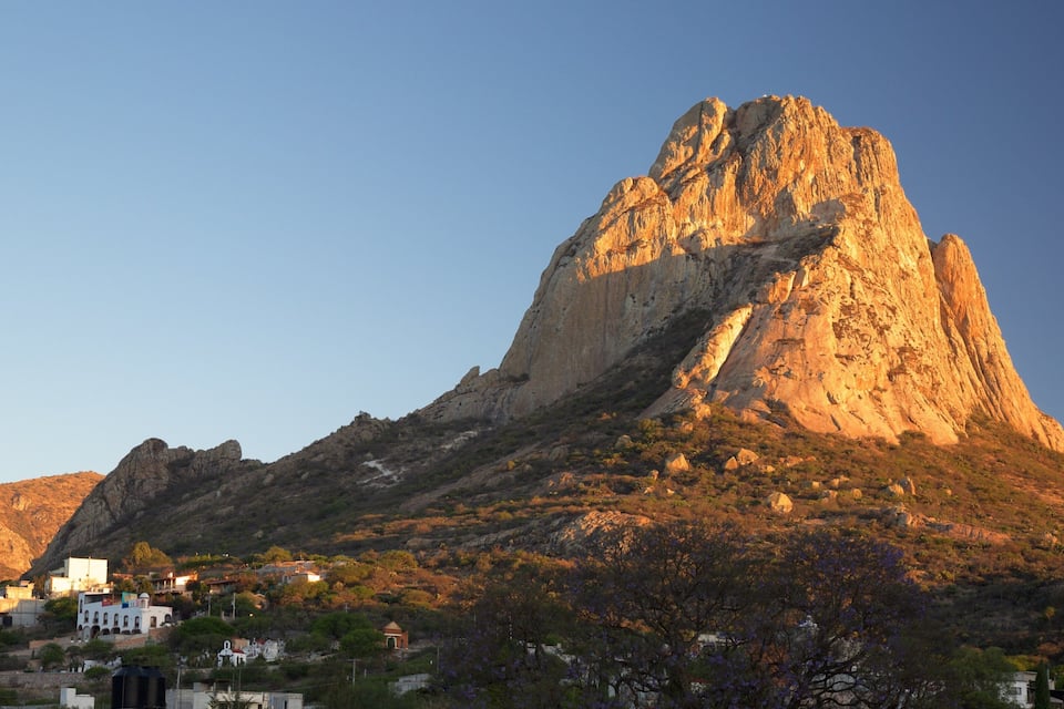 Una montaña con un pico destacado, rodeada por un pueblo con edificios y árboles.